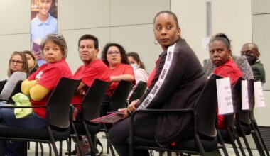 people sit in chairs in a row and look over their shoulders at something out of the frame