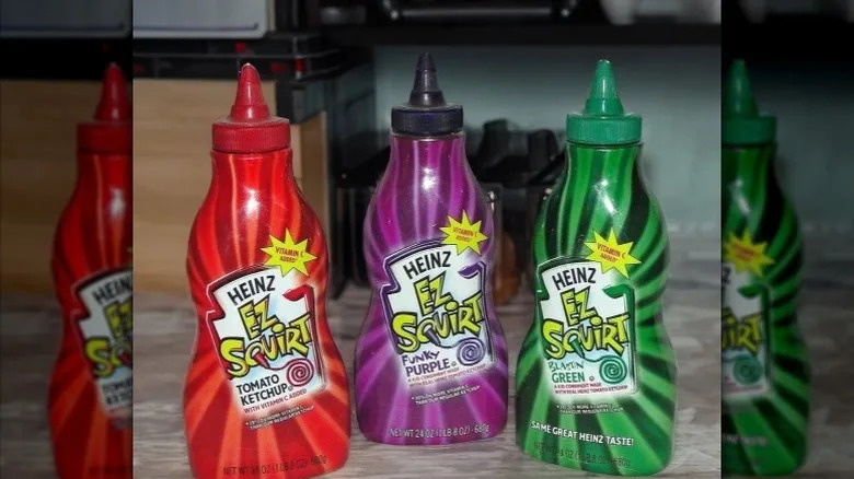 red, purple, and green EZ Squirt ketchup bottles on a kitchen counter