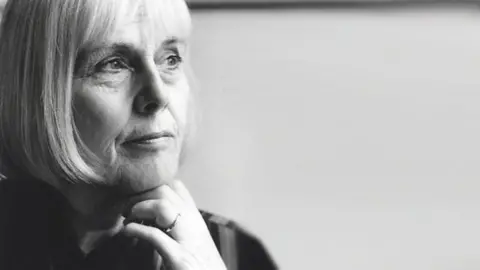 BBC A black and white candid photo of a woman gazing at something away from the camera. There is a ring on her finger