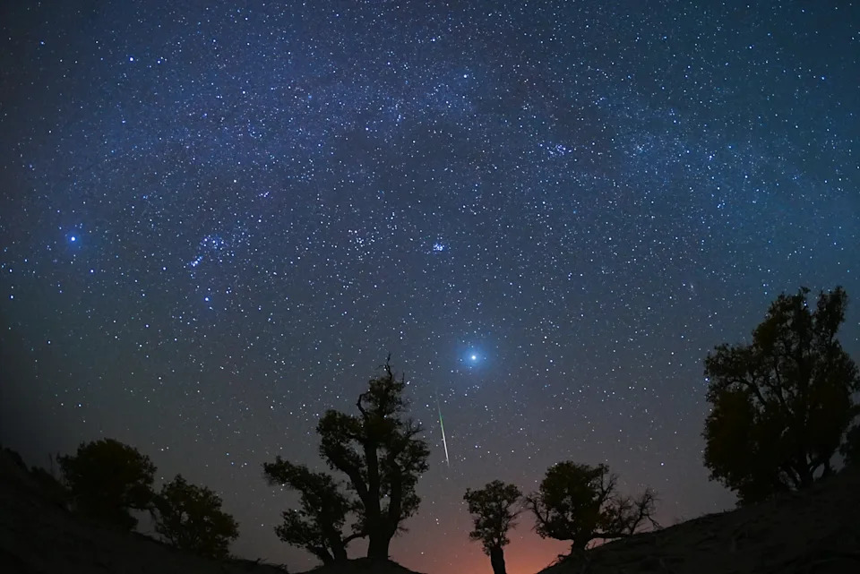 A meteor streaks across the sky over a desert at night.