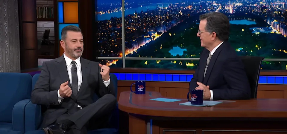 Two talk show hosts sit together on a late-night program set, engaging in conversation
