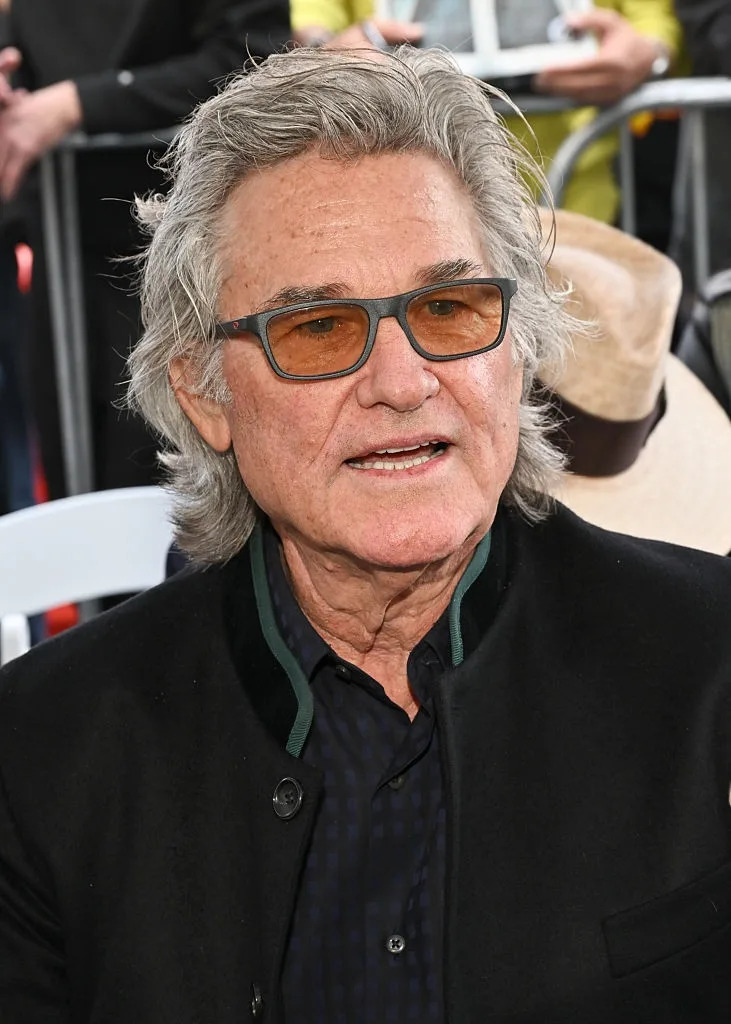 A person with medium-length hair and glasses is wearing a dark jacket and shirt