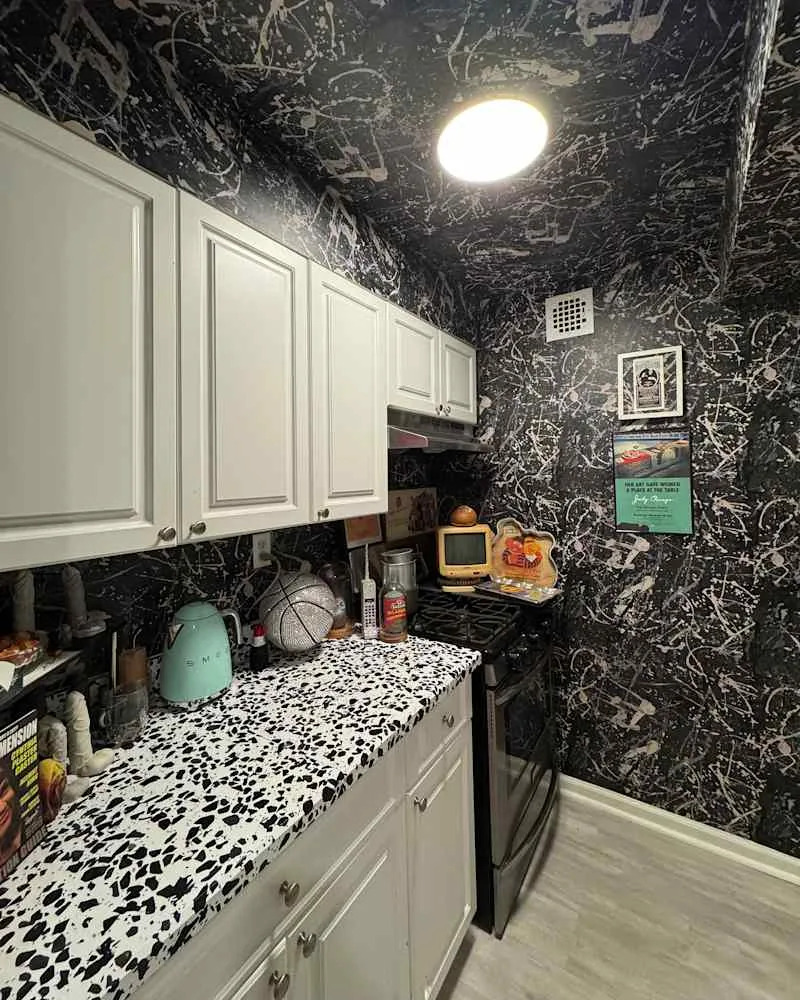 Compact kitchen with black and white splatter wallpaper, white cabinets, a speckled countertop, and retro appliances.