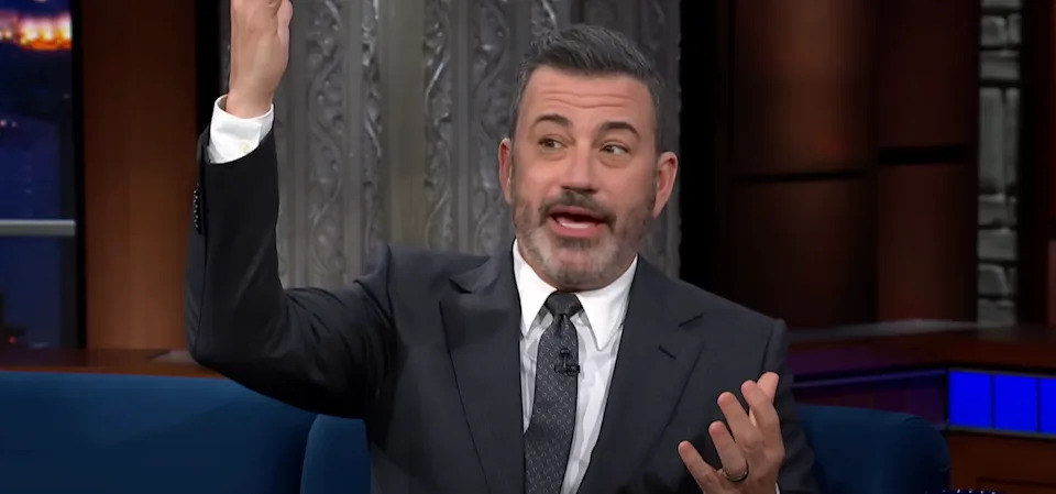 A person in a suit is animatedly talking on a talk show set