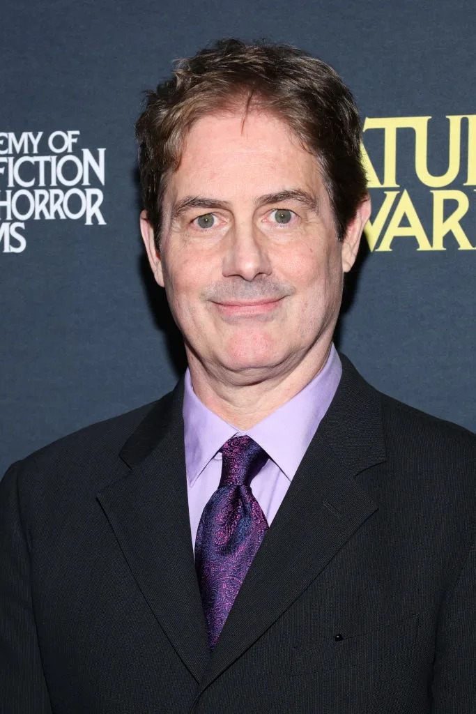 Man in a dark suit and tie on a themed event backdrop