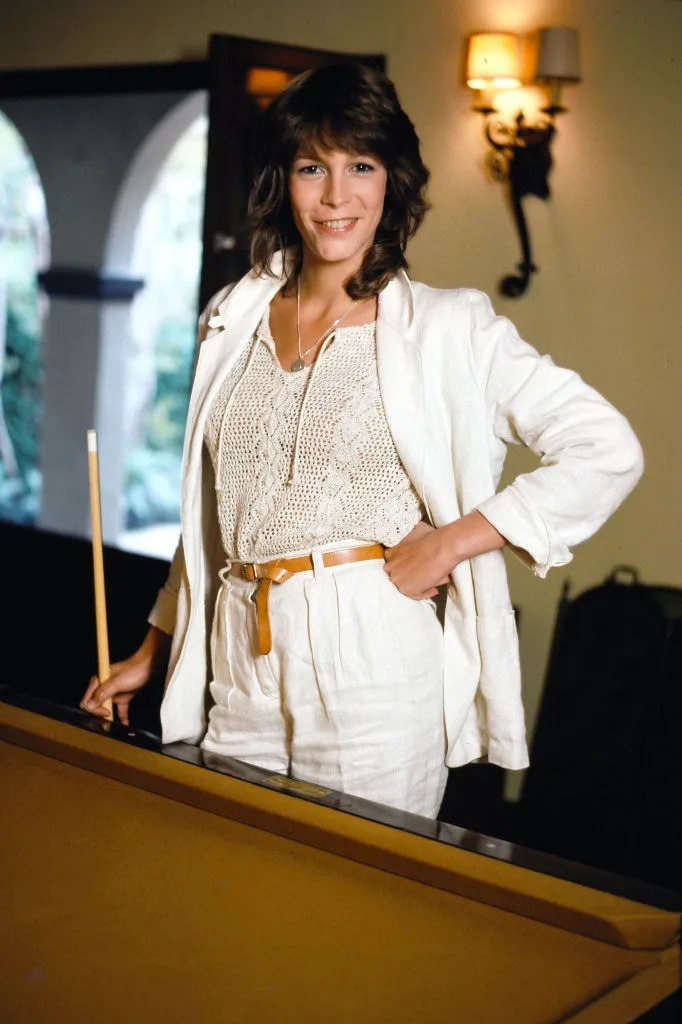 Person in a white suit with a netted top, smiling while standing next to a pool table indoors