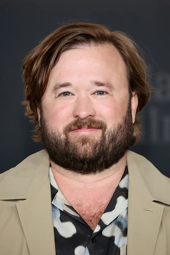 Person in a patterned shirt and light jacket smiling at a media event