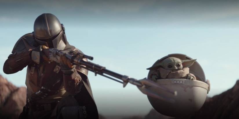The Mandalorian points a gun at Baby Yoda in The Mandalorian.
