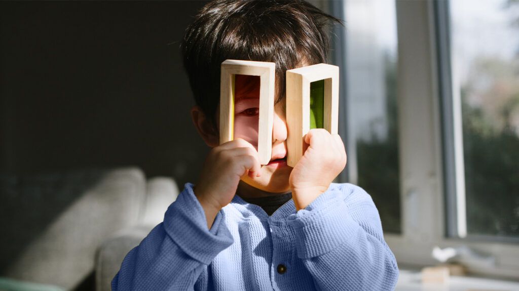 young child looking through two differently coloured plastic pieces, once red, one green