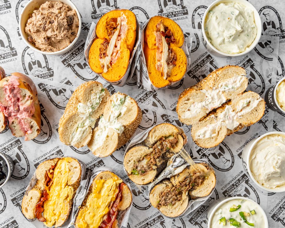 Assorted bagel sandwiches cut in half on a tray with pints of flavored cream cheese