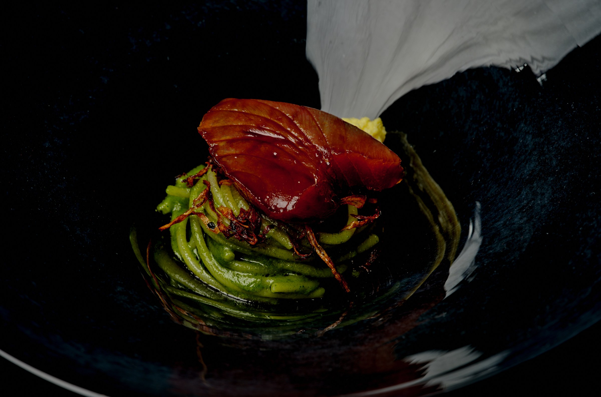 Katsuo atop a bed of pesto spaghetti in a black bowl