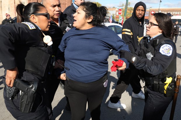 A woman is held by police as angry crowds of people face off with federal agents after a raid at Discount Mall on West 26th Street Chicago's Little Village neighborhood on Oct 23, 2025. (Antonio Perez/Chicago Tribune)