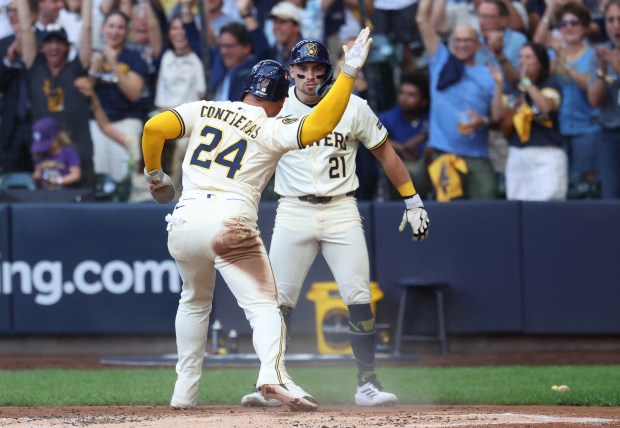 Milwaukee Brewers catcher William Contreras (24) and teammate Caleb Durbin (21) celebrate after Contreras scored on an error by Chicago Cubs second baseman Nico Hoerner in the first inning of the NL Division Series Game 1 at American Family Field in Milwaukee on Oct. 4, 2025. (Chris Sweda/Chicago Tribune)