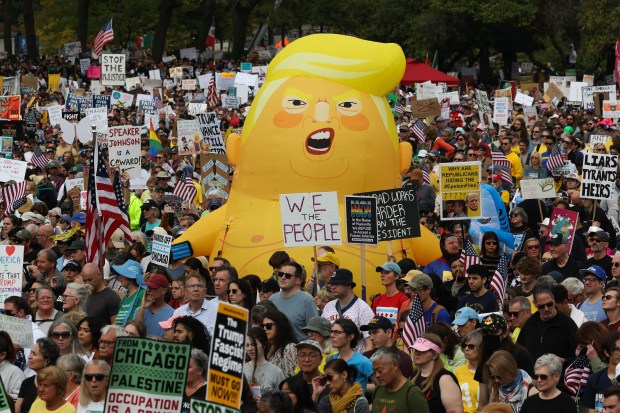 A balloon depicting Donald Trump looms above demonstrators as they listen to speakers during the "No Kings" rally at Butler Field Saturday, Oct. 18, 2025, in Chicago. (John J. Kim/Chicago Tribune)