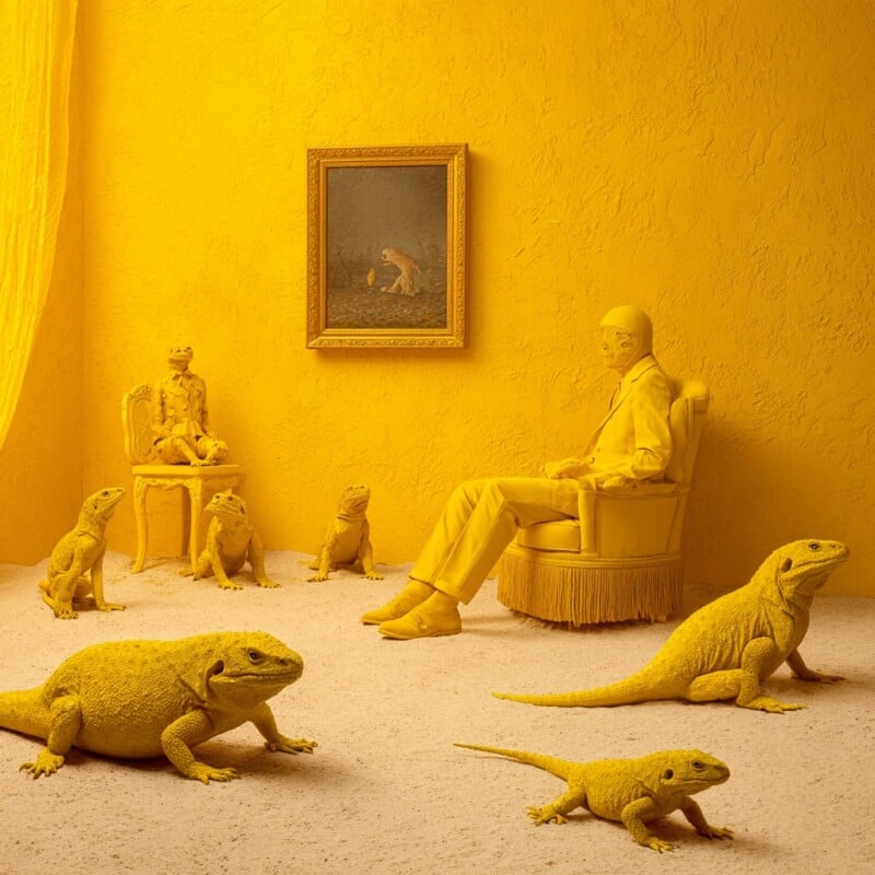 A person dressed in yellow sits in a yellow room surrounded by several large yellow lizards. There is a yellow-framed painting of a lizard on the wall, and all furniture and décor are yellow, creating a monochromatic scene.