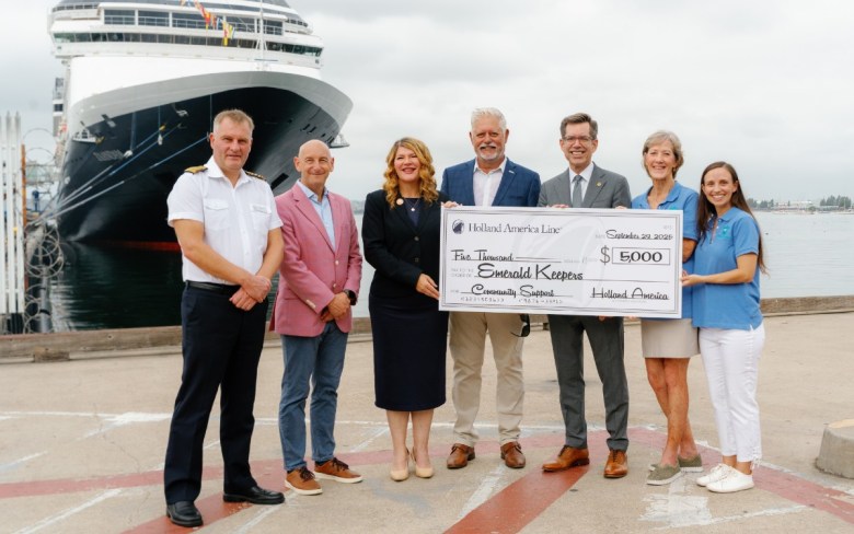 A group of seven people holding a large check in front of a docked cruise ship.