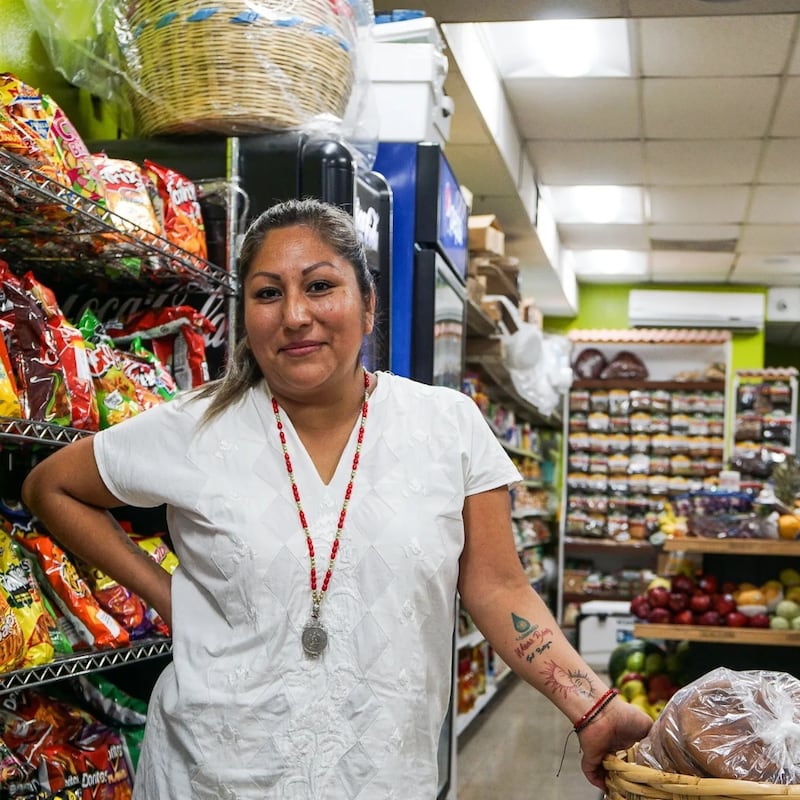 Photo of a woman posing inside a store with chips and fruits behind her.