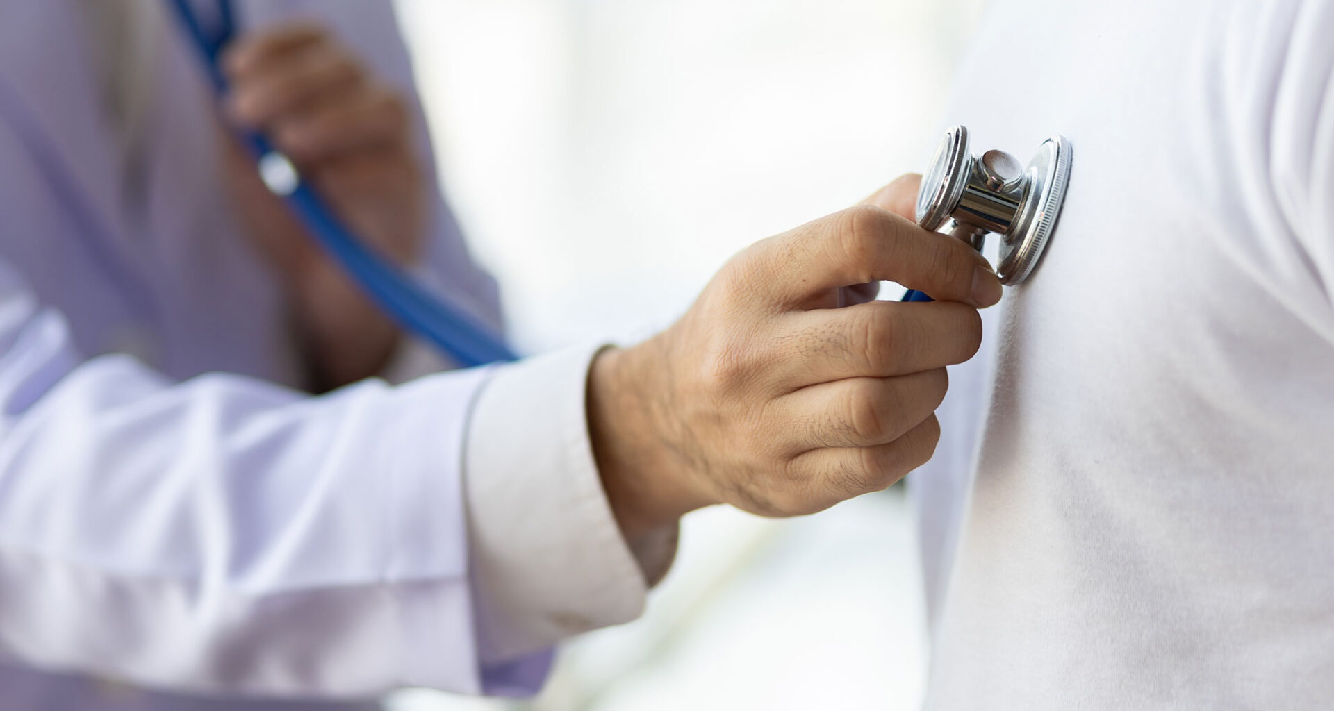Doctor using stethoscope examining male patient.