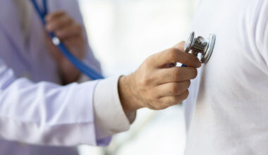 Doctor using stethoscope examining male patient.