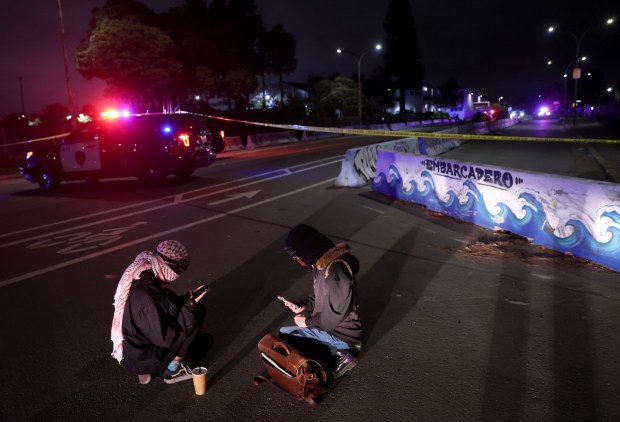 Protesters sit outside the perimeter while police investigate after shots were fired near the Coast Guard Island entrance in Oakland, Calif. on Thursday, Oct. 23, 2025. U.S. Coast Guard police opened fire on a U-Haul truck after it backed up a ramp at the entrance to the Alameda island, where U.S. Customs and Border Patrol agents have been based. (Jane Tyska/Bay Area News Group)