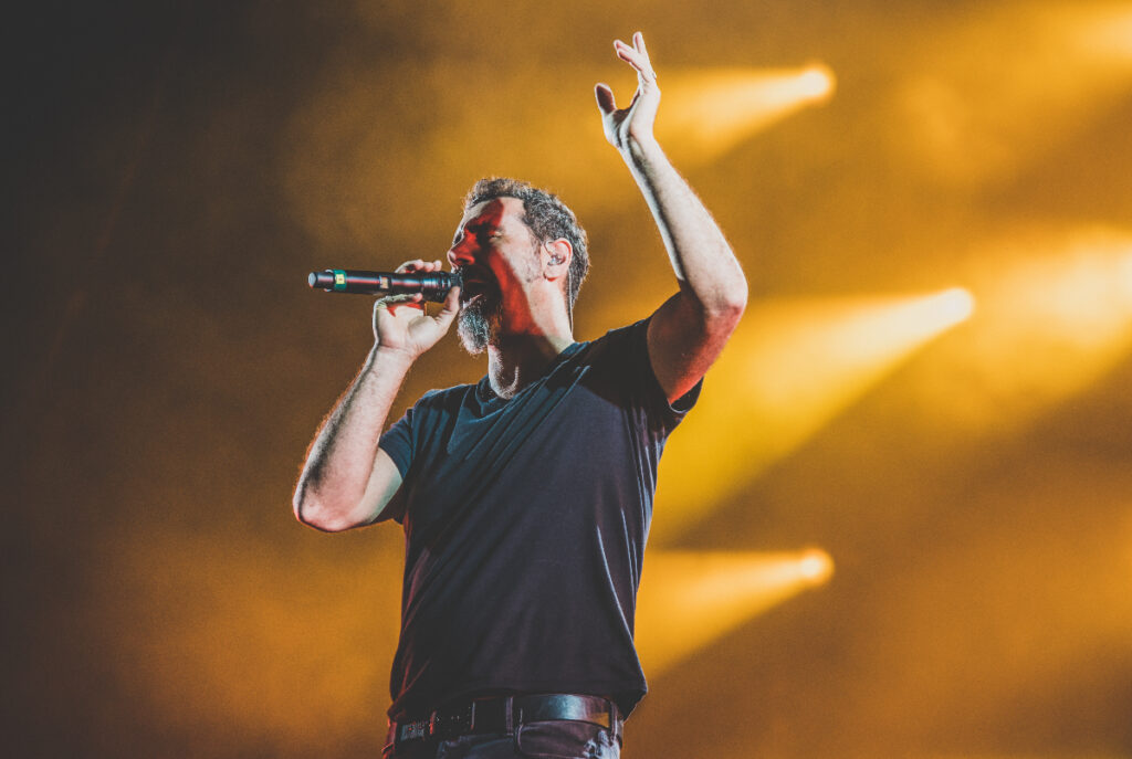 Image shows System of a Down frontman, Serj Tankien, performing on stage.