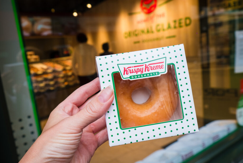 Image shows someone holding up an individually packaged Krispy Kreme donut.