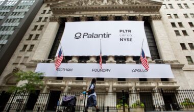 A mail carrier wearing a protective mask passes a banner displaying Palantir Technologies Inc. signage during the company's initial public offering (IPO) in front of the New York Stock Exchange (NYSE) in New York, U.S., on Wednesday, Sept. 30, 2020.