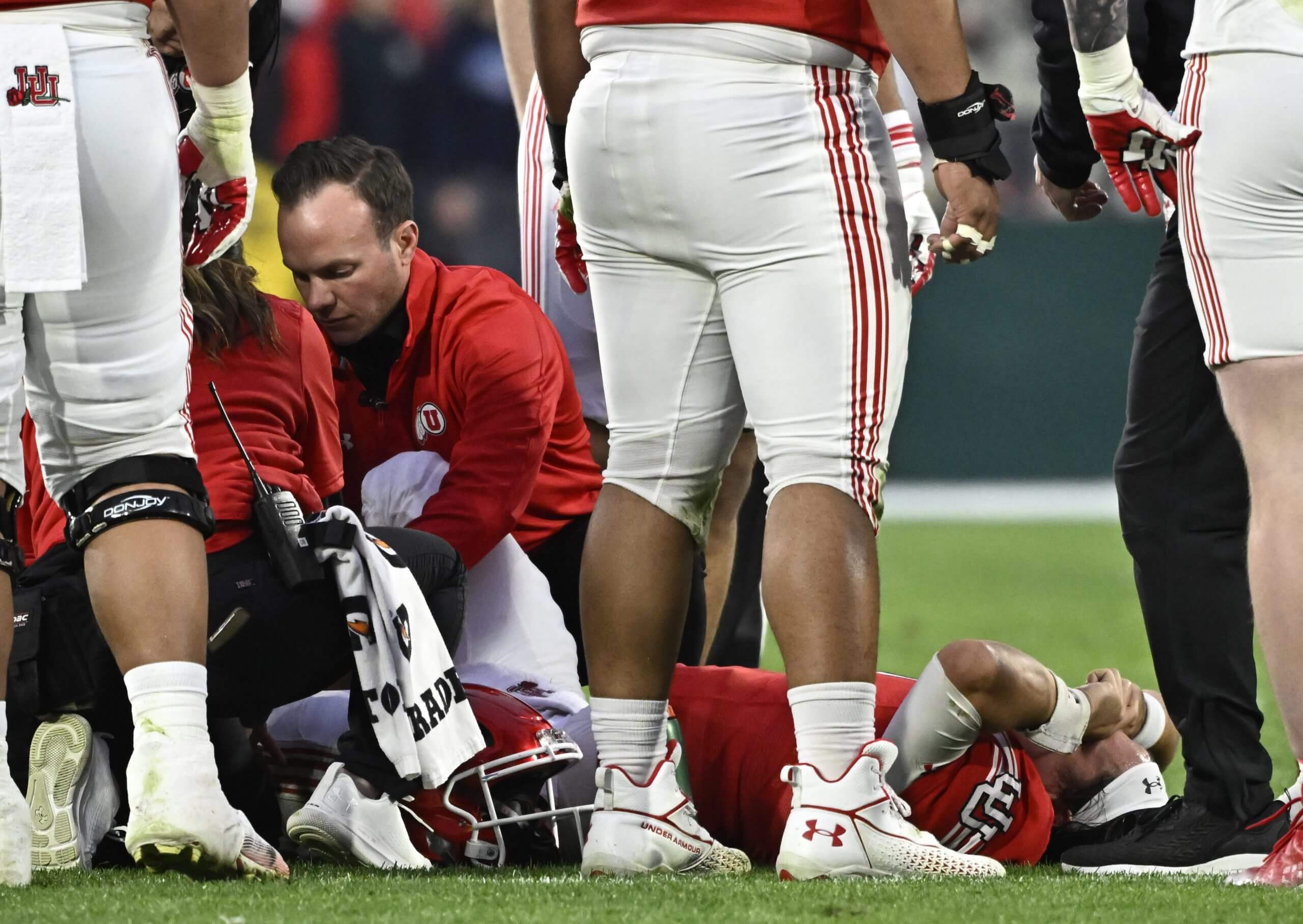 Cam Rising lies on the football field with hands to his face after an injury