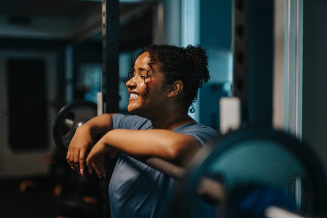 Smiling young woman leaning on barbell at health club