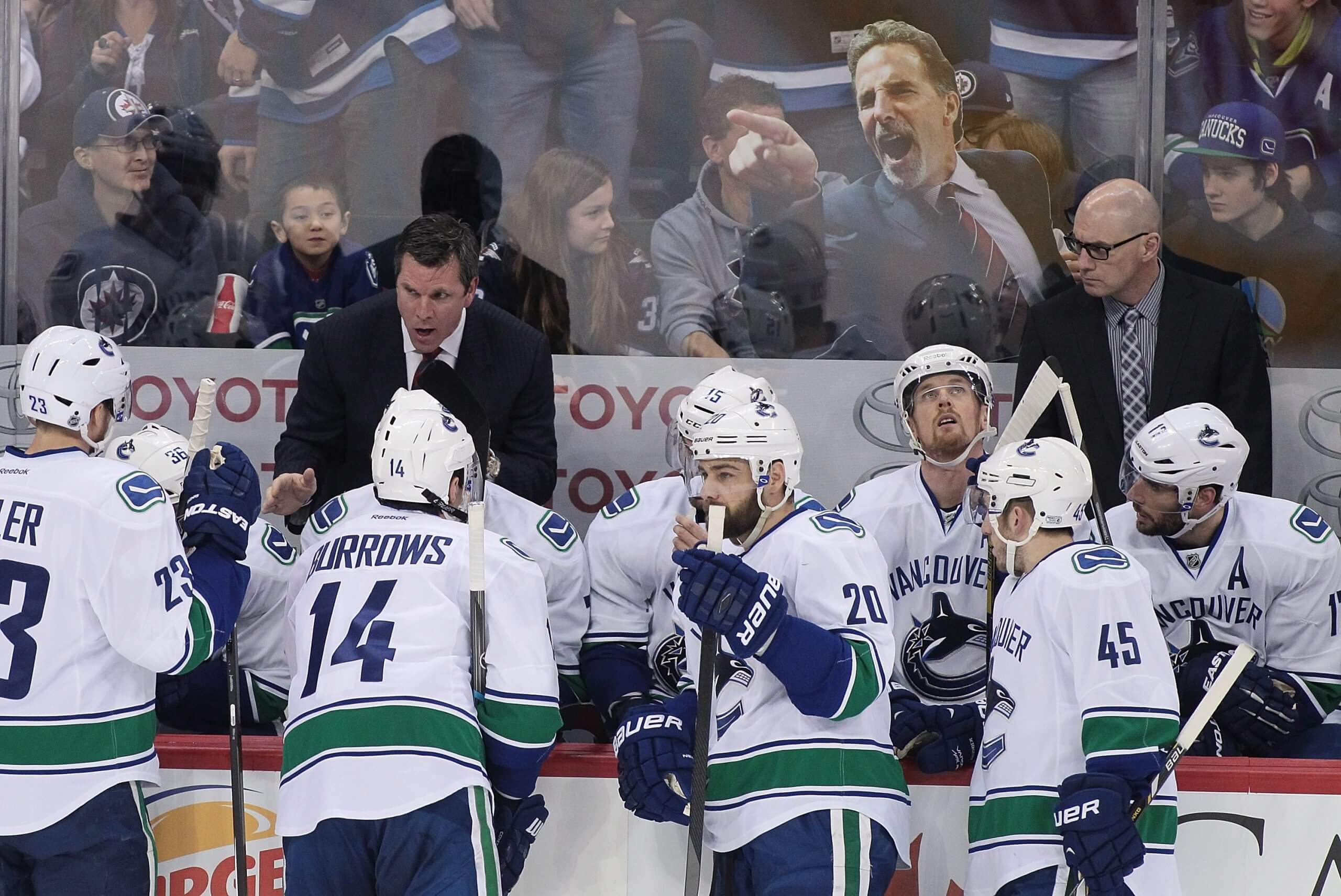 A fan holds a cardboard cutout of a yelling John Tortorella behind the Vancouver Canucks bench.