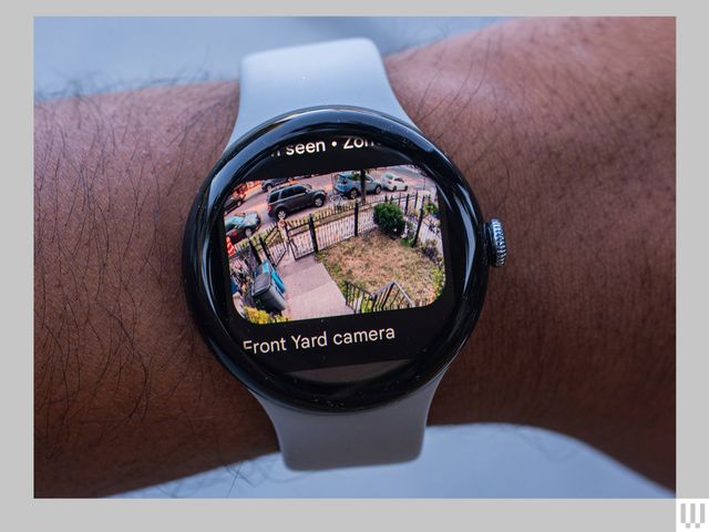 Person's wrist wearing a smart watch with the screen showing video footage of a front yard camera