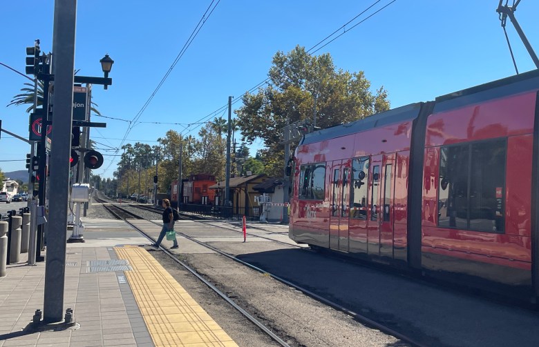 A light rail car at a stop on tracks on a city street.