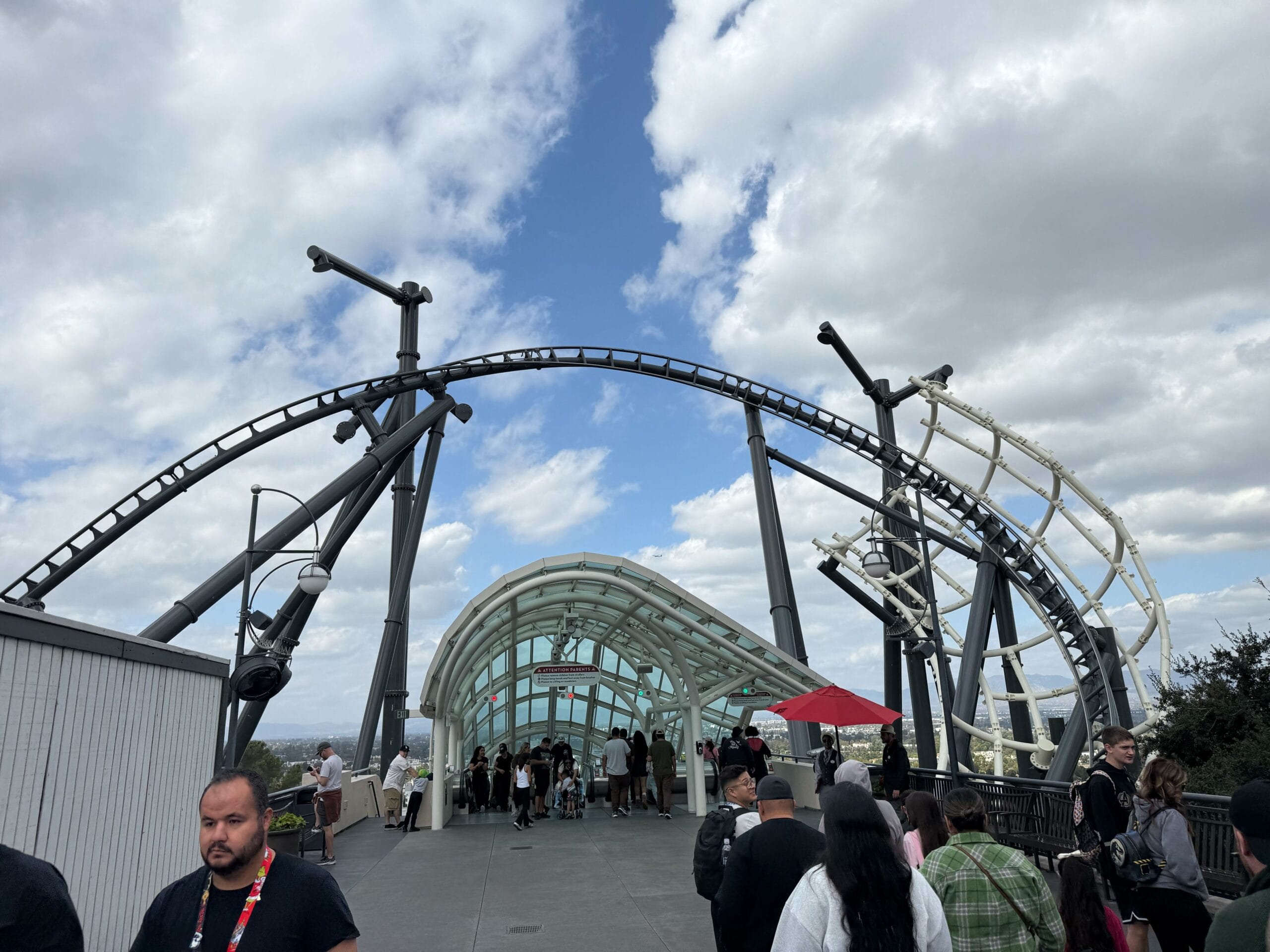 Guests queue beneath a twisting roller coaster track at a Disney park, the partly cloudy sky adding to the lively atmosphere.