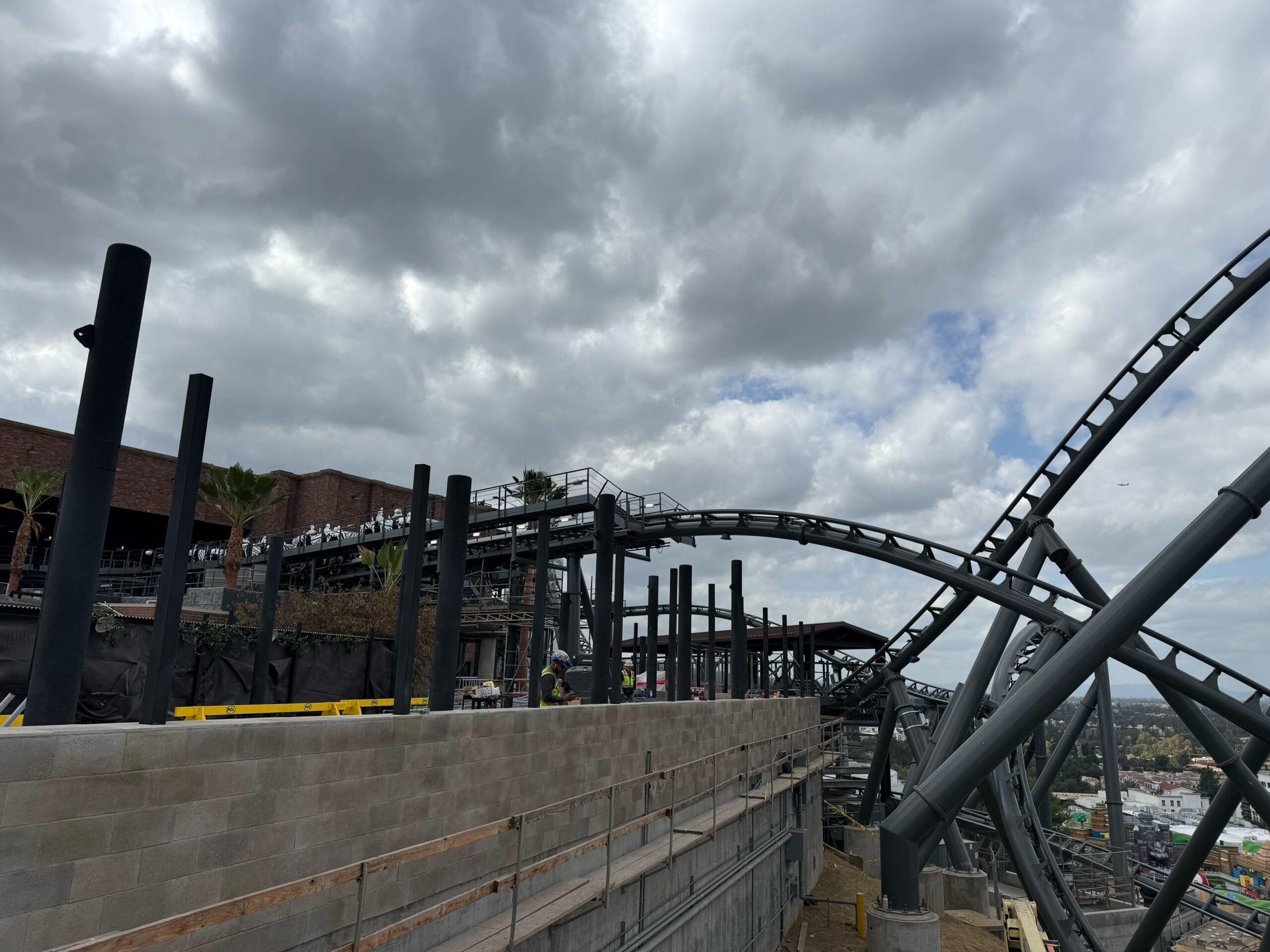 A roller coaster track curves beneath a cloudy sky near a construction site, reminiscent of new attractions at Disney parks.