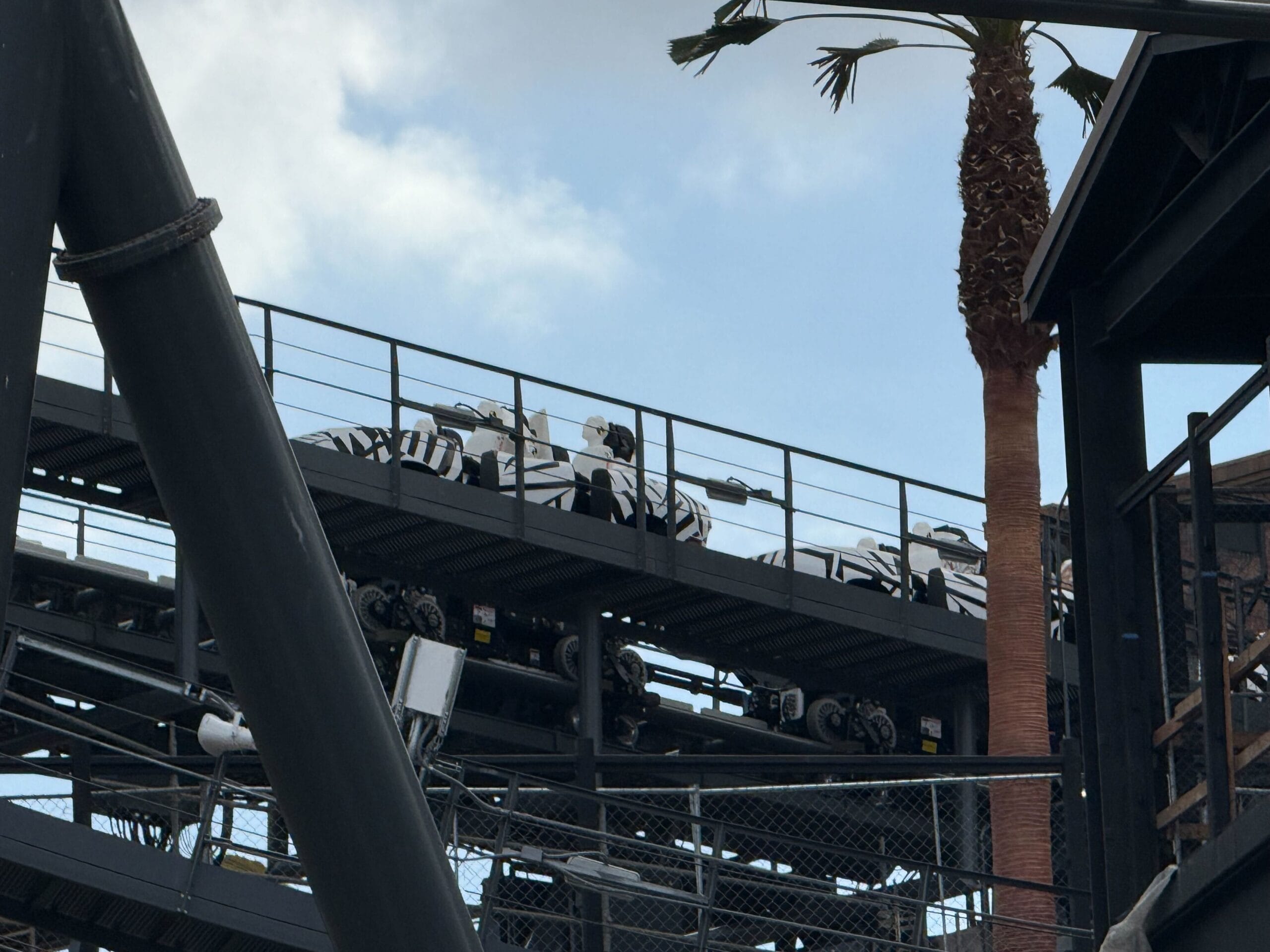 A Stormtrooper-themed roller coaster train sits on an elevated track by a palm, evoking Disney’s immersive Star Wars park design.