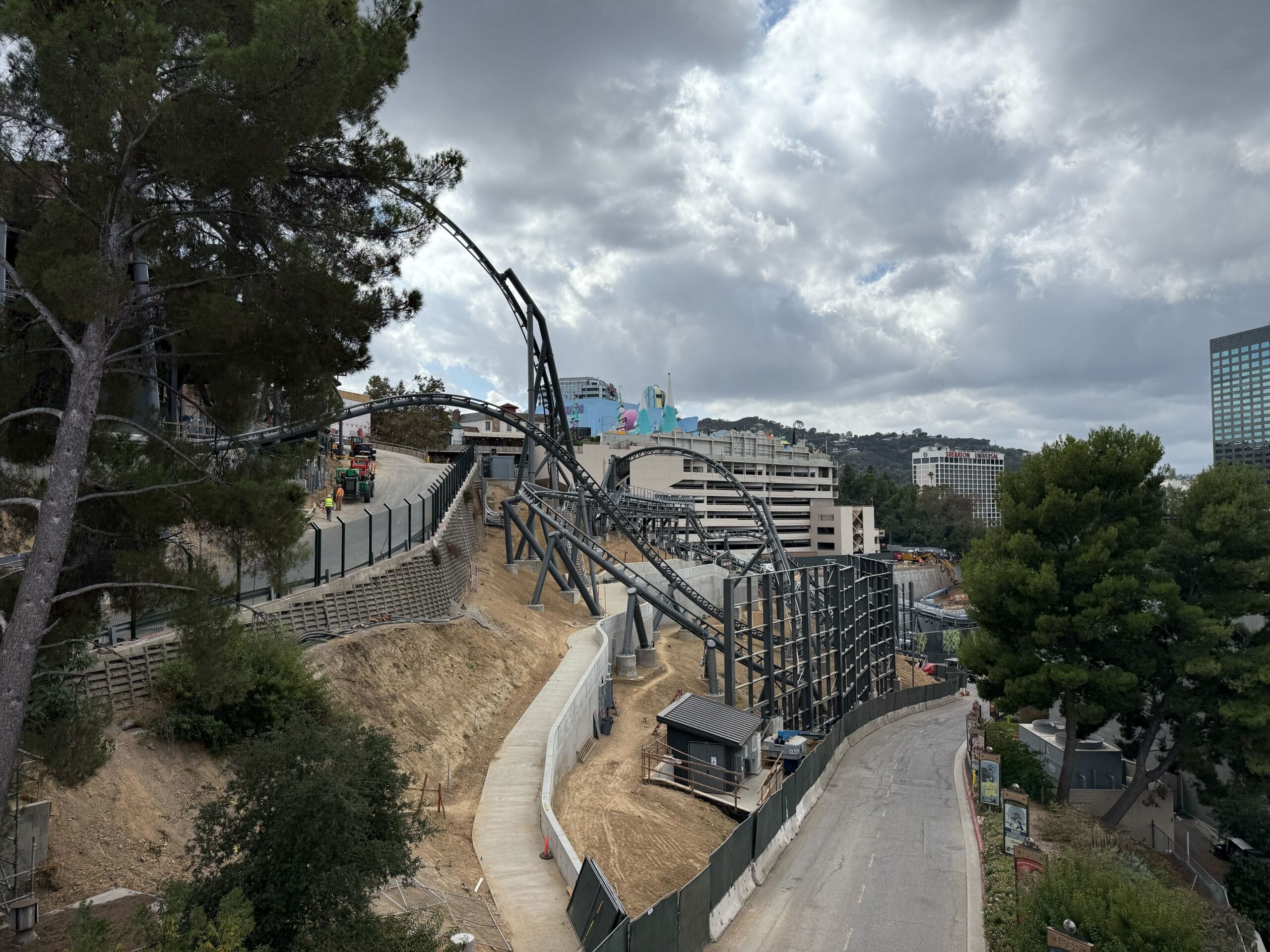A steel roller coaster under construction winds through a hillside, with cloudy skies and distant buildings—not a Disney castle in sight.