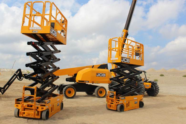 JCB 32 foot and 42 foot scissor lifts in the foreground, with a straight boom and a telescopic forklift behind them at the JCB manufacturing plant site near Palo Alto Road on Oct. 16, 2025. The scissor lifts have accordion-like struts that allow them to grow upwards. The telescopic forklift and straight boom are four-wheel vehicles with extendable arms.