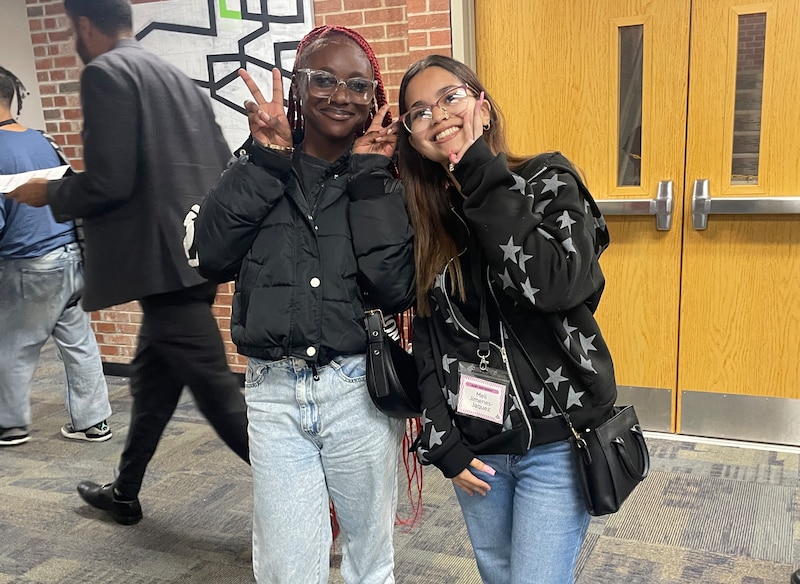Two female students with dark jackets pose together.