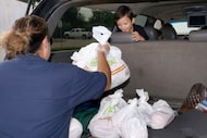 Dallas Independent School District staff member Lisa Sepeda loads bags of food into the...