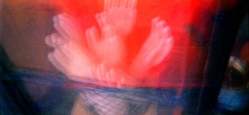 A cluster of white rubber gloves appears layered and blurred, creating a ghostly effect against a background of vivid red and blue hues. The scene is abstract, with soft, overlapping shapes and a basket visible below the gloves.