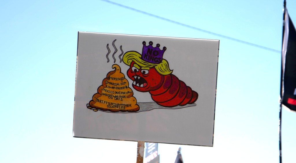 a protester holds a sign with a bug-shaped donald trump eating a pile of poop