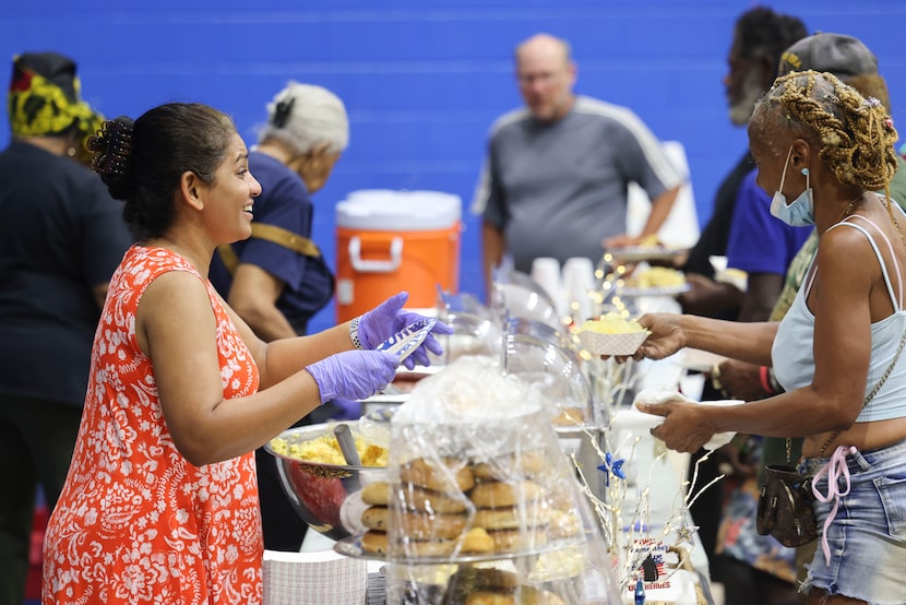 Staff Vera Isaac (left) serves as people walk in during a hot meal program at Dallas...