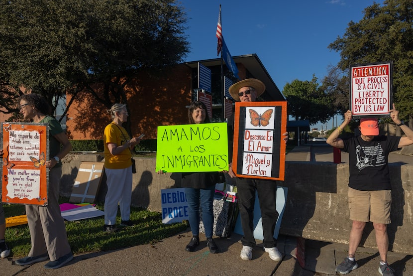 Chris and Holly McGowan (center) hold signs Monday reading "We love immigrants" and "Rest in...