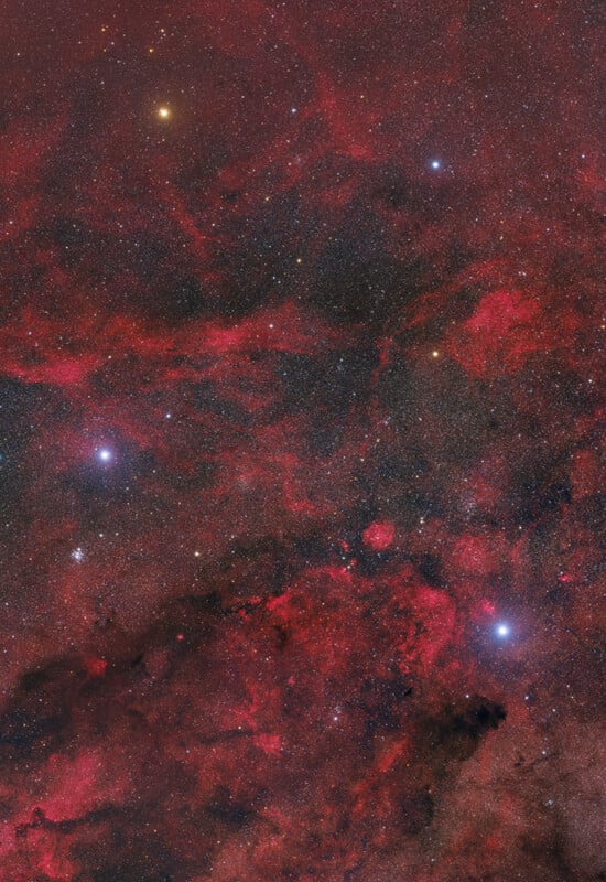 A vibrant image of a star-filled night sky featuring bright stars and glowing red nebula clouds, creating a colorful and detailed cosmic scene.