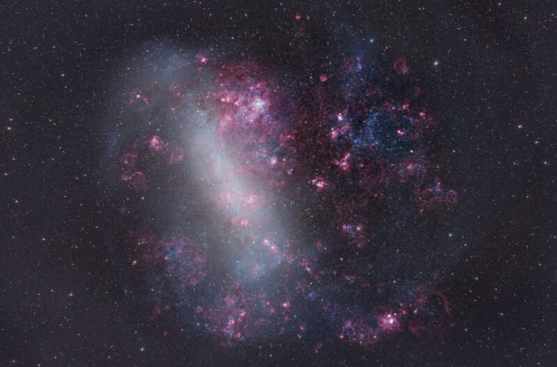 A colorful galaxy filled with bright pink, purple, and blue regions, glowing nebulae, and dense star clusters against a dark, star-filled background.