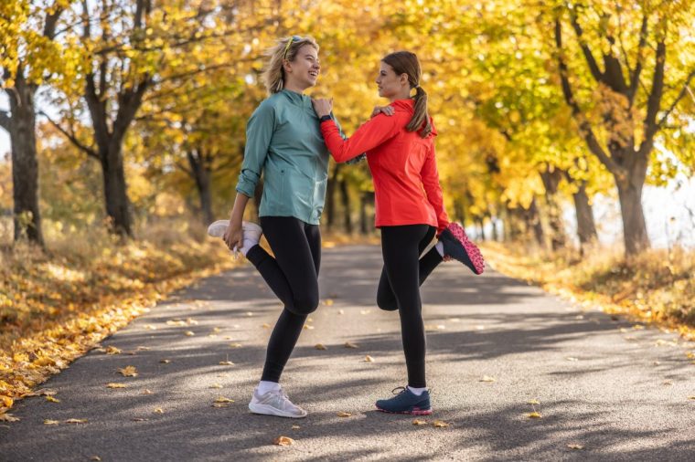 Sporty female athletes are warming up before jogging, doing lower body stretching in the park.