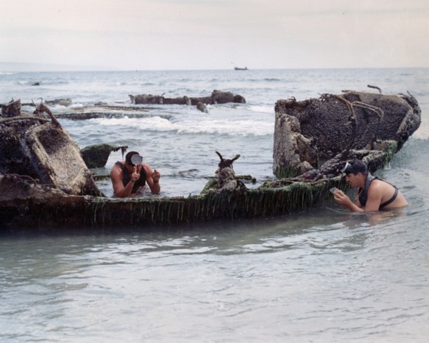 Two U.S. Navy SEALs conduct hydrographic readings near a shipwreck on Silver Strand Beach in the 1960s. The diver on the right is holding a slate and wax pencil to transcribe the readings from the SEAL on the left. (National Navy UDT-SEAL Museum)