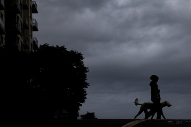 A person walking a dog crosses Ash Street under dark clouds on Tuesday in San Diego. (Meg McLaughlin / The San Diego Union-Tribune)