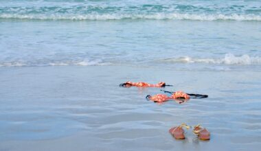 A pair of sandals and a floral bikini lie on the wet sand near the shoreline, with gentle ocean waves approaching in the background.