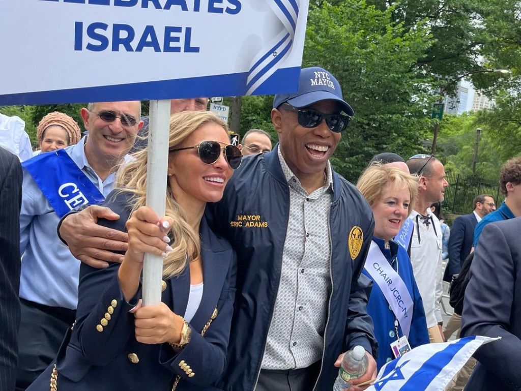 Eleonora Srugo holding a sign with a man with his arm around her, and Eric Adams smiling beside her.